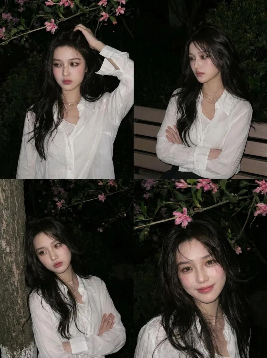 A young Asian woman stands beneath pink blossoms at night