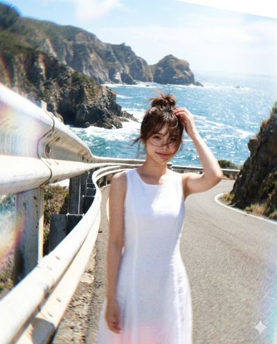 A woman smiles by a guardrail on a windy coastal road