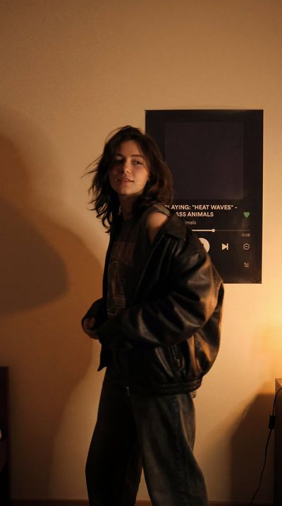 A woman in a leather jacket turns her head in warm amber light