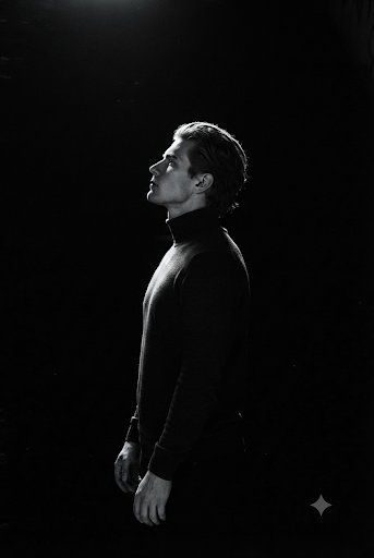 Profile of a solemn man in a dark turtleneck under a spotlight