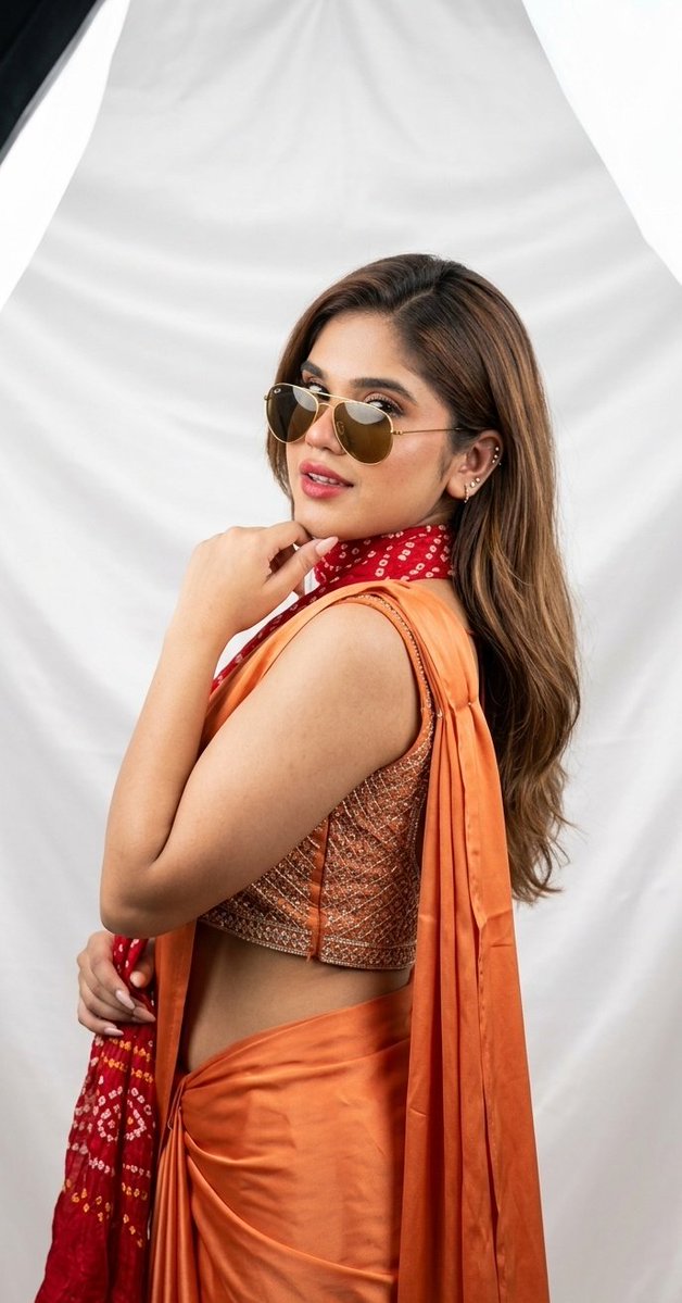 Woman in orange saree turns back with flowing hair and sunglasses