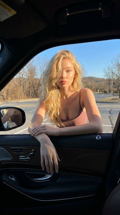 Golden sunlight illuminates a blonde woman leaning from a luxury car window.