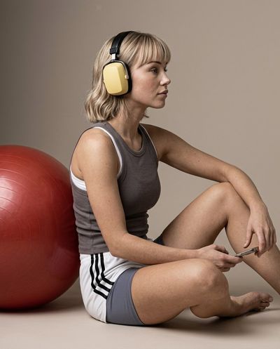 Young woman in profile sits against red exercise ball with headphones