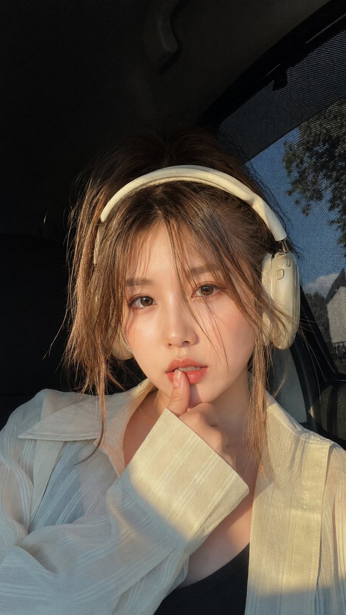 Young woman with headphones touches her lip in golden sunlight