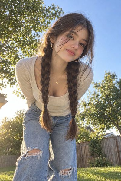 Teenage girl with braided pigtails smiles in sunlit backyard at golden hour