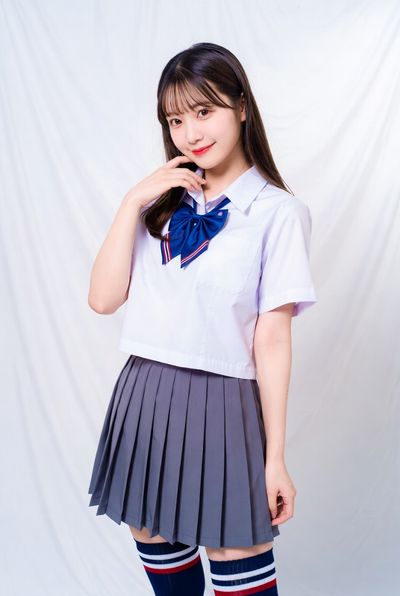 A young student in a pleated skirt poses thoughtfully in a studio.