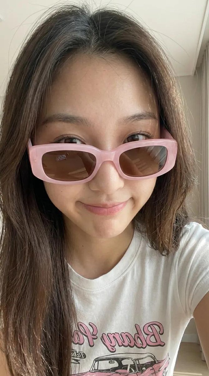 Young woman in pink sunglasses poses with relaxed confidence indoors