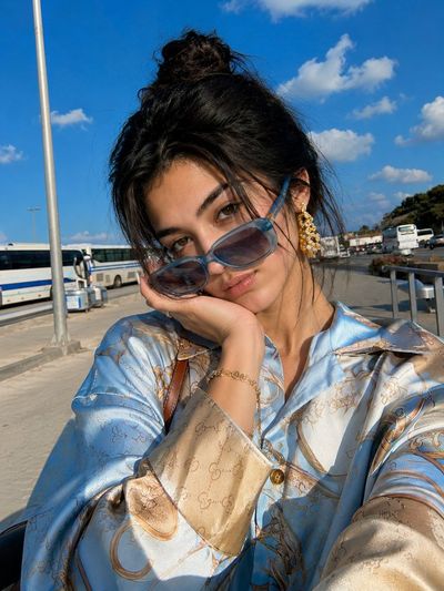 A woman in oversized sunglasses smirks under bright sunlight