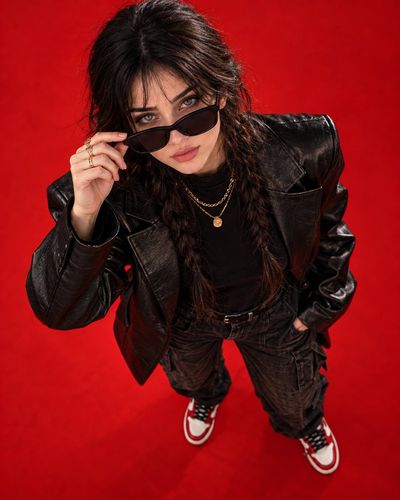 Confident Woman Adjusts Sunglasses Against Vibrant Red Studio Background
