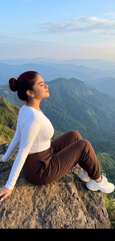 A woman sits on a cliff edge enjoying mountain views at sunrise