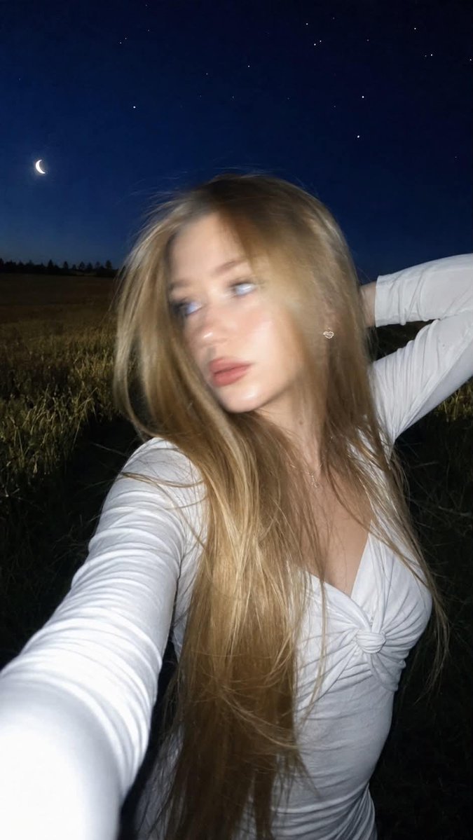 A woman takes a candid night selfie with motion blur in a field