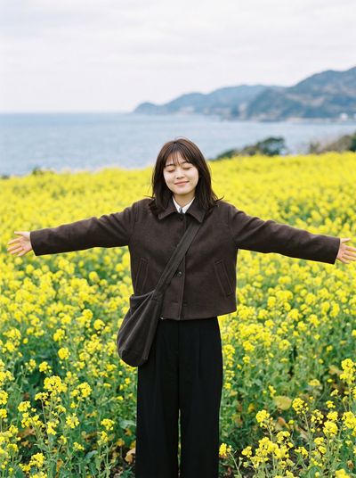 Joyful woman embraces blooming canola field by tranquil sea