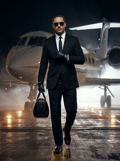 A wealthy man in a black suit walks from a private jet hangar at night.