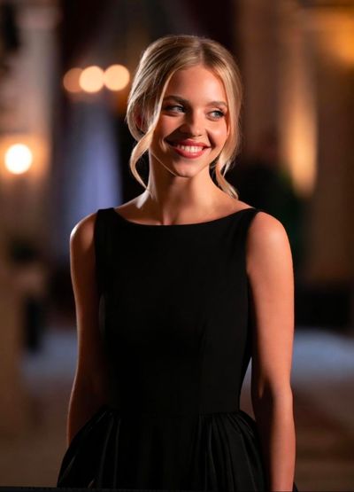 A blonde woman in a black beaded gown smiles softly at a gala.