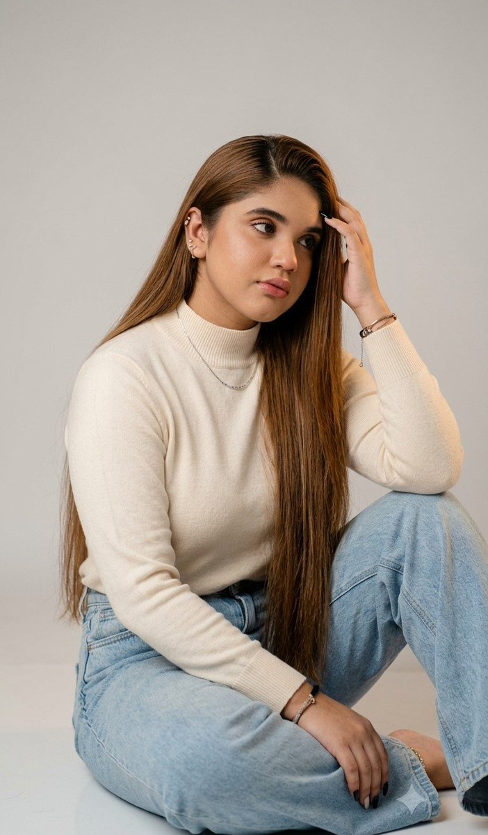 A young woman in white bustier sits thoughtfully in soft studio light