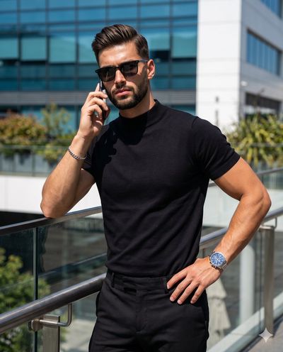 Confident businessman in black sunglasses leans against metal railing