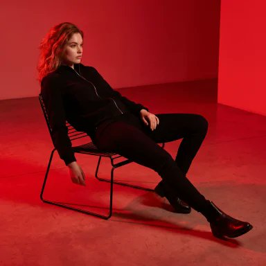 A confident woman in black reclines on a metal chair