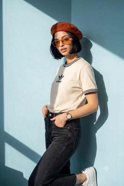 Woman in cream tee and orange beret leans against pastel blue wall