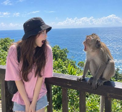 Woman and macaque monkey mimic shocked expressions on ocean overlook