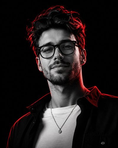 A confident young man stares intensely under neon red rim lighting.