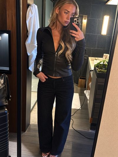 Blonde woman in black jacket takes mirror selfie in luxury hotel bathroom