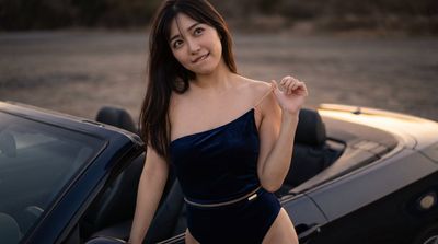 Woman laughs beside black car in golden hour light