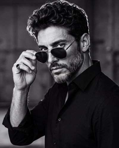 Man in black shirt lifts aviator sunglasses with ring hand