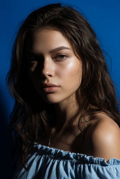Young woman with wavy brown hair in dramatic portrait lighting.
