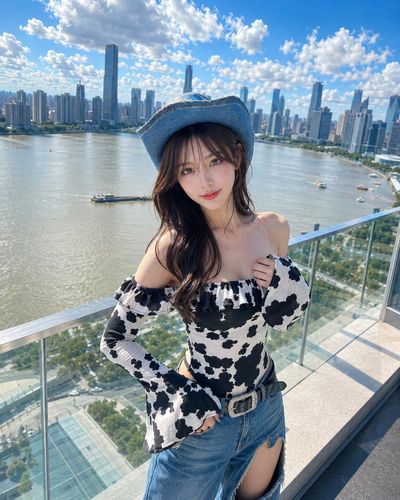 A K-pop idol poses on a luxury hotel balcony in a cow-print romper.