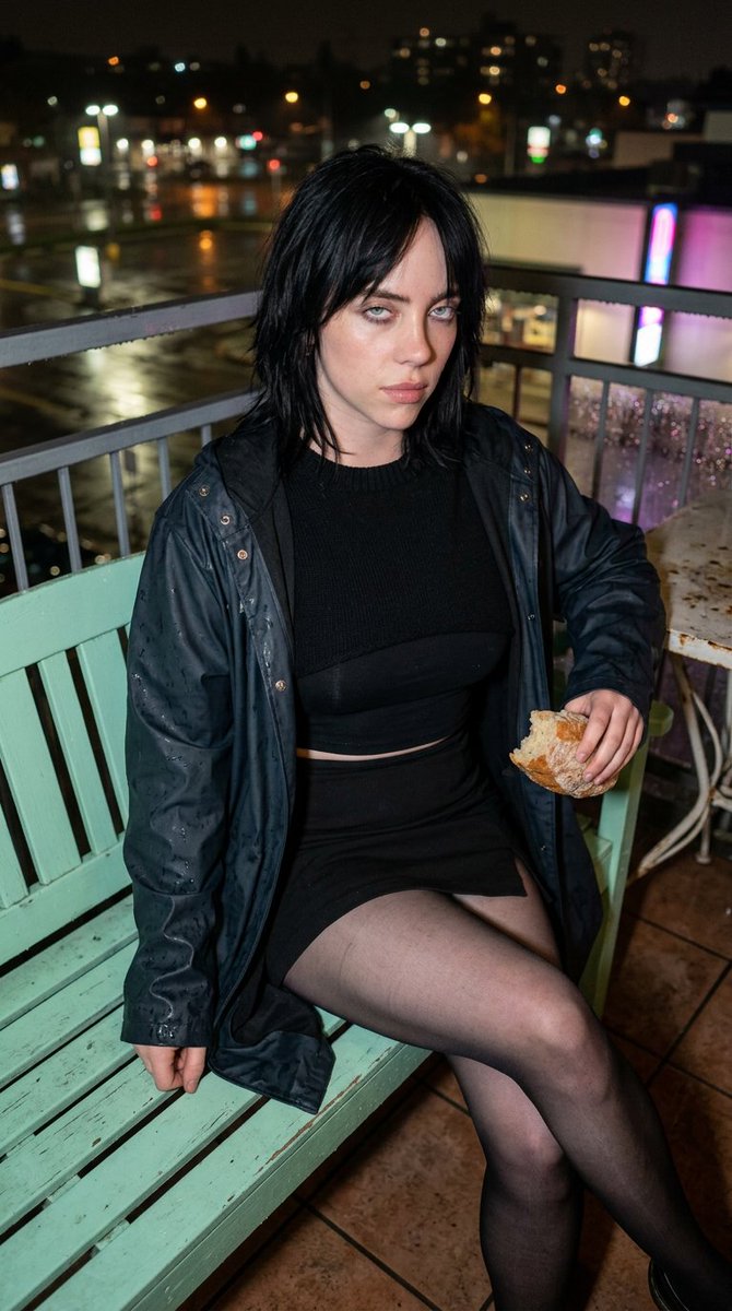 Billie Eilish poses on a rain-wet balcony at golden hour